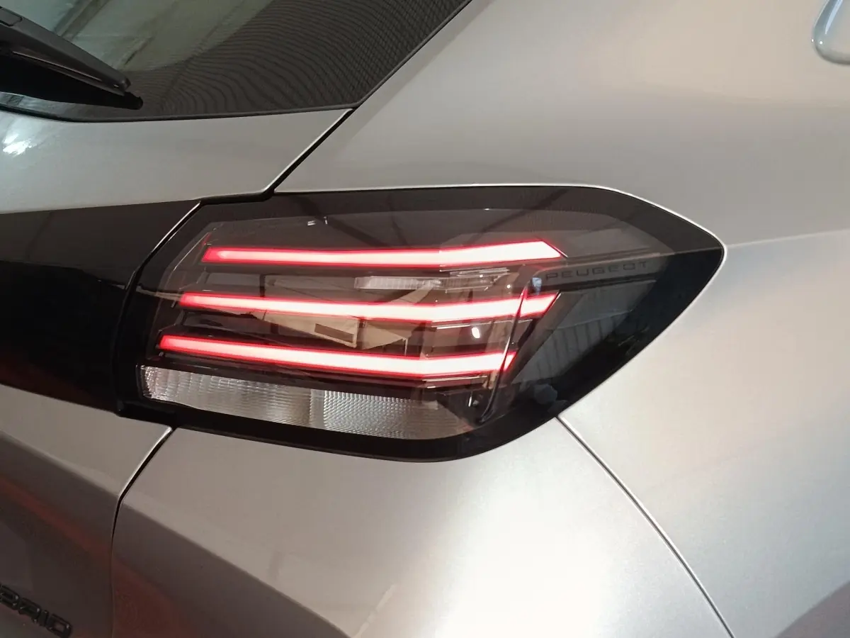 Gros plan sur le feu arrière droit allumé d'une Peugeot 208 Hybrid gris clair, soulignant son design moderne et lumineux.