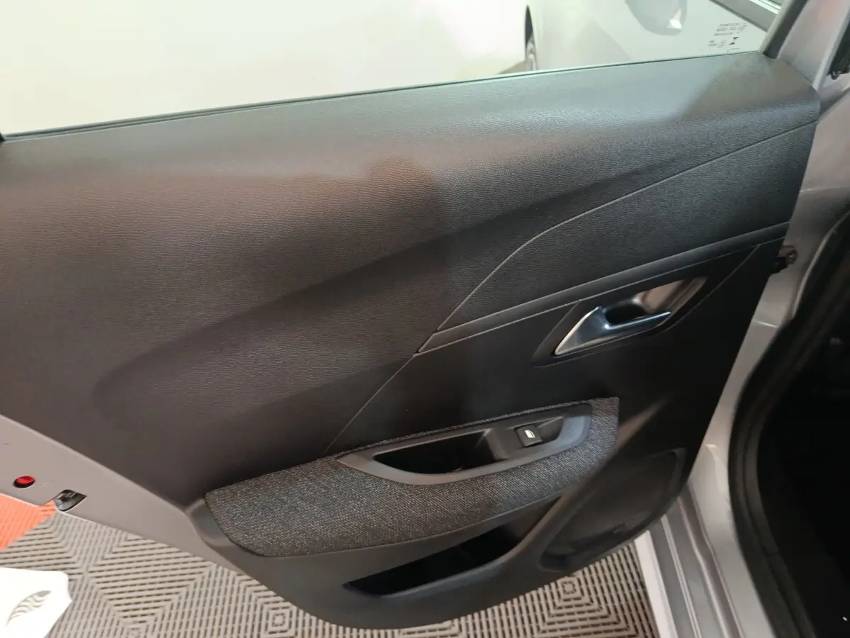Vue intérieure sur la porte arrière droite d'une Peugeot 208 Hybrid gris clair, avec accoudoir tissu et commande de vitre.