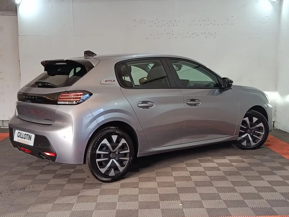Vue 3/4 arrière droite d’une Peugeot 208 Hybrid gris clair avec jantes noires et badge Style sur l’aile arrière.