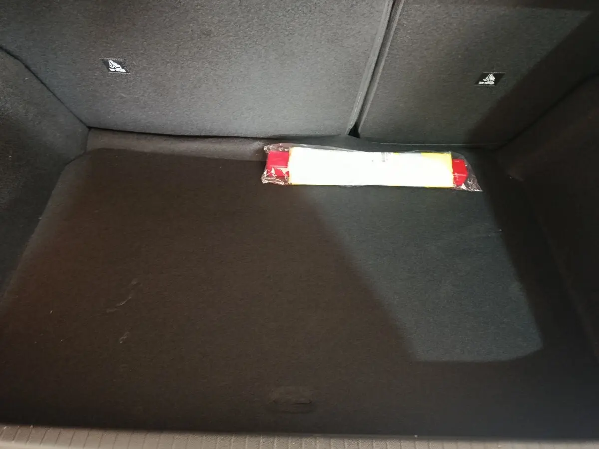 Coffre vide de Peugeot 208 Hybrid gris clair, vue intérieure montrant la moquette noire et un triangle de signalisation.