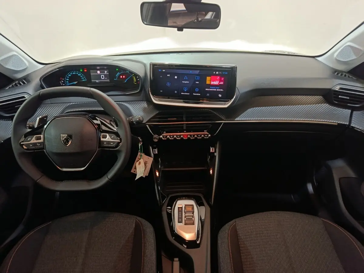 Vue intérieure frontale du tableau de bord et volant cuir noir de la Peugeot 208 Hybrid 2025 avec écran tactile central.