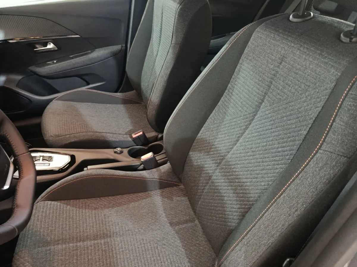 Vue intérieure rapprochée des sièges avant gris foncé avec surpiqûres orange du Peugeot 208 Hybrid 100 e-DCS6 Style 2025.