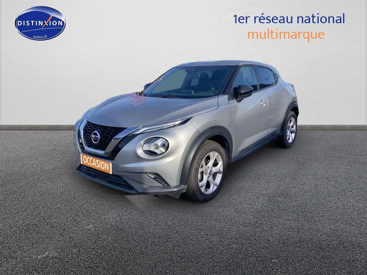 Nissan Juke gris clair vu en 3/4 avant droit, mettant en valeur ses phares ronds et sa calandre noire distinctive.