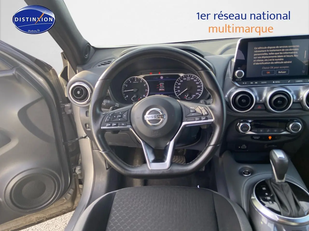 Vue intérieure centrée sur le volant et le tableau de bord d'un Nissan Juke gris clair avec boîte automatique.