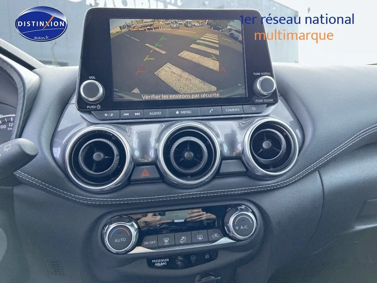 Tableau de bord du Nissan Juke gris clair 2021 avec écran de caméra de recul et commandes de climatisation visibles.