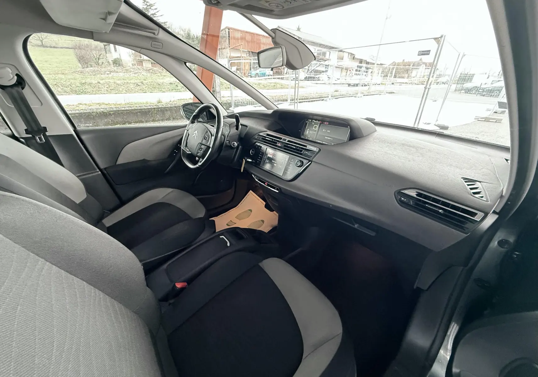 Vue intérieure côté conducteur de la Citroën C4 Picasso gris platinium, montrant tableau de bord et sièges bicolores noirs et gris.