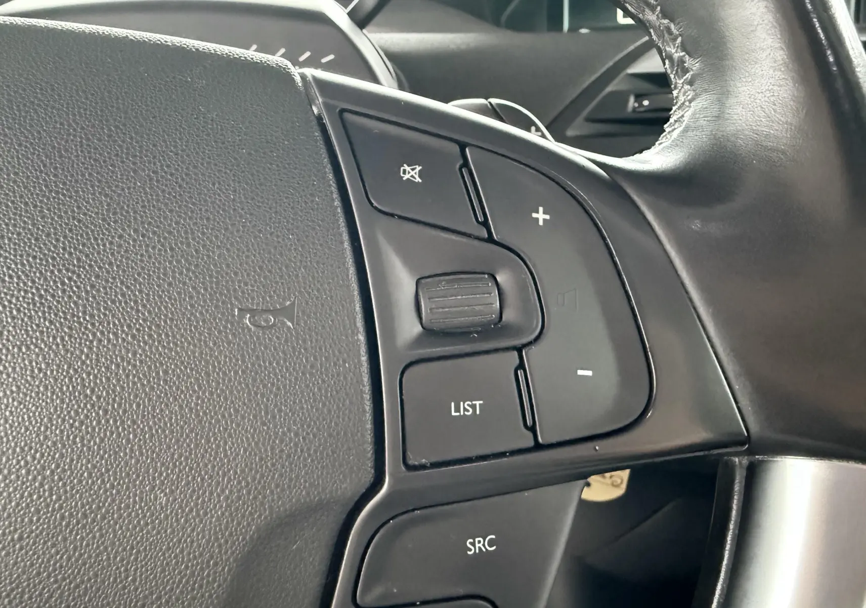Gros plan sur les commandes au volant en cuir noir de la Citroën C4 Picasso 2015, côté gauche.