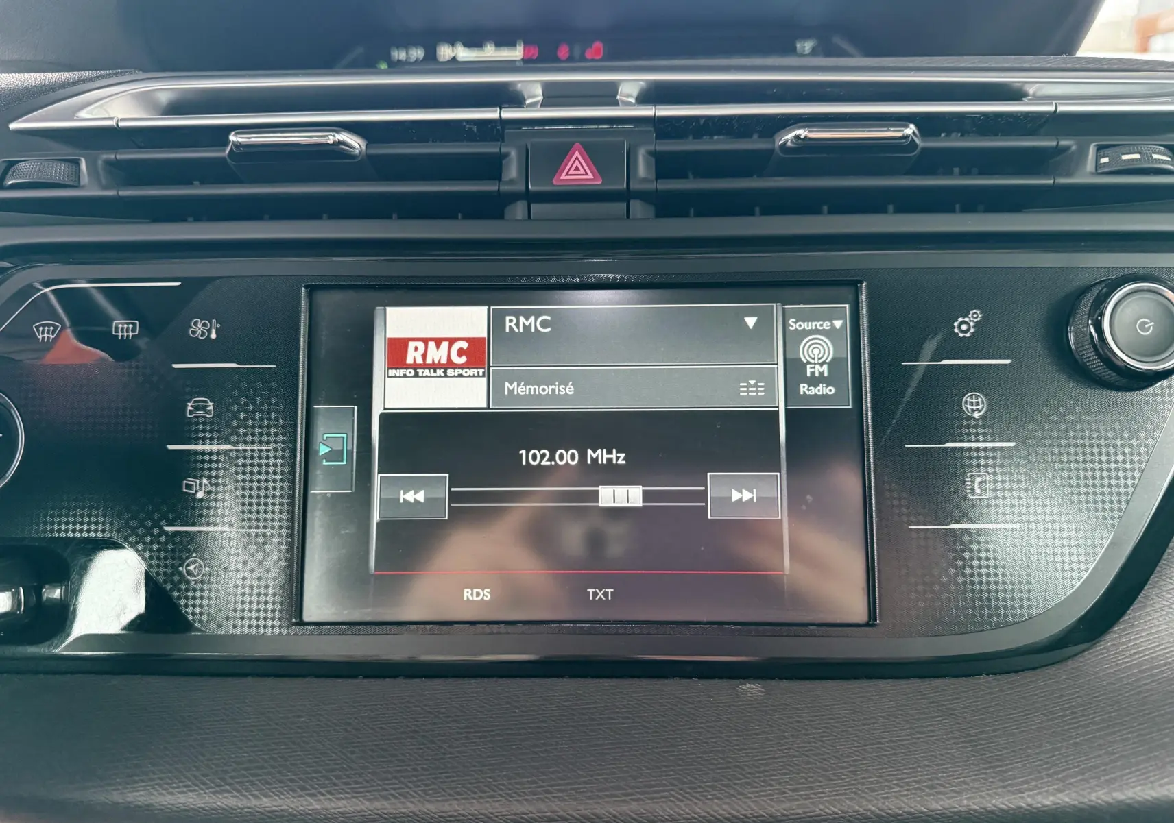 Vue rapprochée du tableau de bord de la Citroën C4 Picasso 2015, écran central affichant la radio RMC sur fond noir.