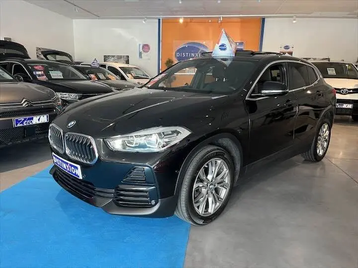 BMW X2 noir métal vue 3/4 avant droit en showroom avec toit ouvrant et jantes alliage visibles