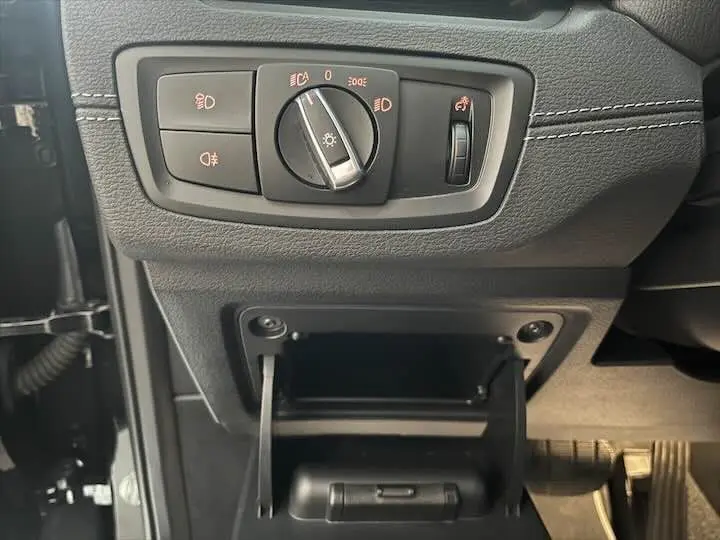Détail intérieur côté gauche du tableau de bord noir du BMW X2 2022 montrant les commandes d'éclairage et un petit rangement ouvert.