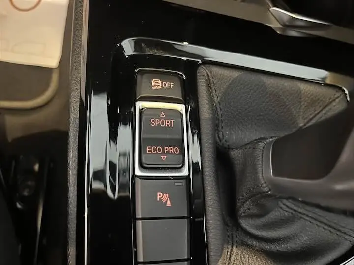 Gros plan sur les commandes de modes de conduite et assistance au stationnement dans une BMW X2 noire, intérieur cuir noir.