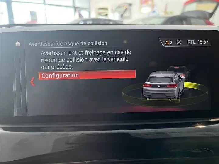 Écran intérieur affichant l'alerte de risque de collision avec représentation graphique d'un BMW X2 noir métal vue arrière.