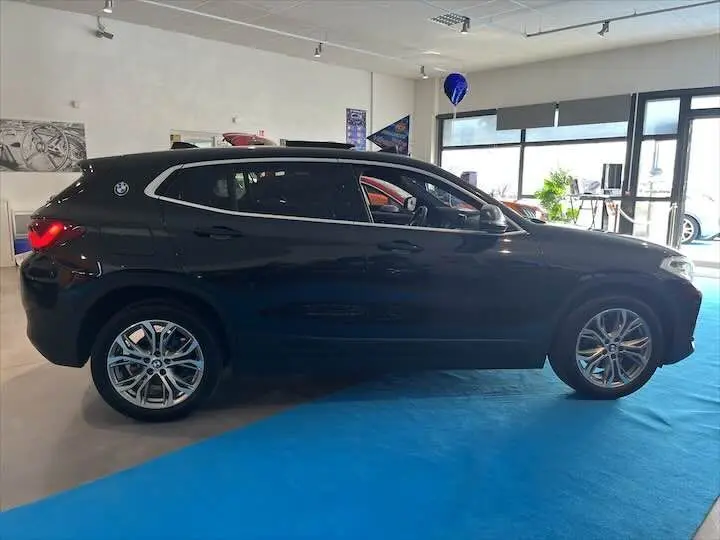 Profil côté gauche d'un BMW X2 noir métal 2022 en showroom, avec jantes alliage et toit ouvrant visible.
