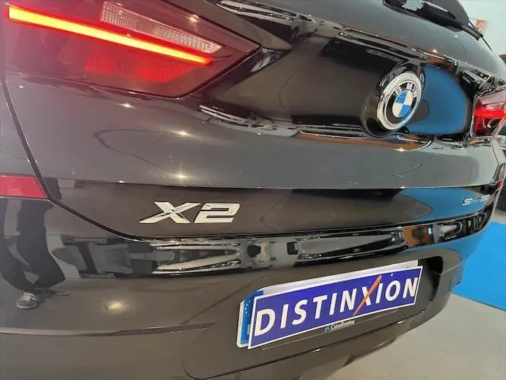 Vue rapprochée arrière droite d’un BMW X2 noir métal avec logo et plaque Distinxion visible