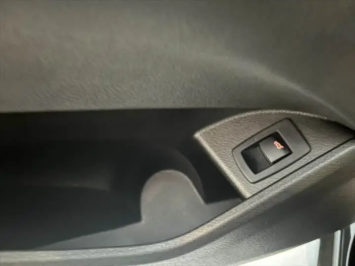Bouton de déverrouillage du coffre sur la porte intérieure d'une BMW X2 noir métal, vue rapprochée.