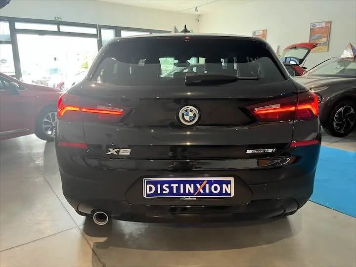 Vue arrière d'un BMW X2 noir métal sDrive 18i 2022 avec feux LED allumés et plaque Distinxion en concession.