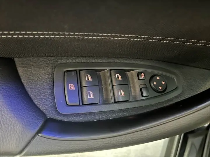 Gros plan sur les commandes électriques des vitres et rétroviseurs côté conducteur d'une BMW X2 noir métal 2022.