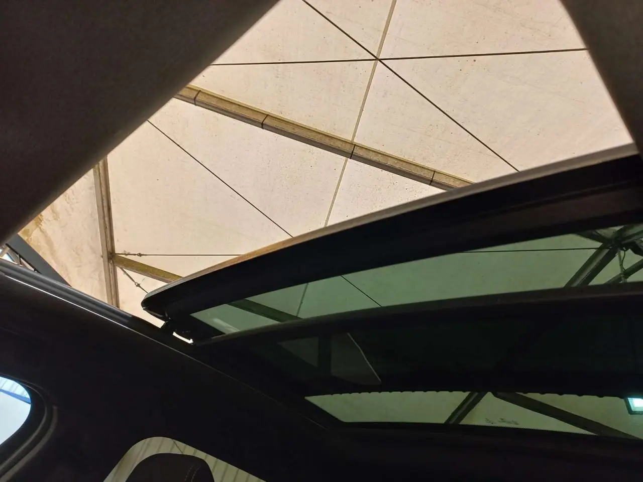 Toit ouvrant panoramique ouvert vu de l'intérieur sur BMW X2 noir métal, sous une tente blanche.