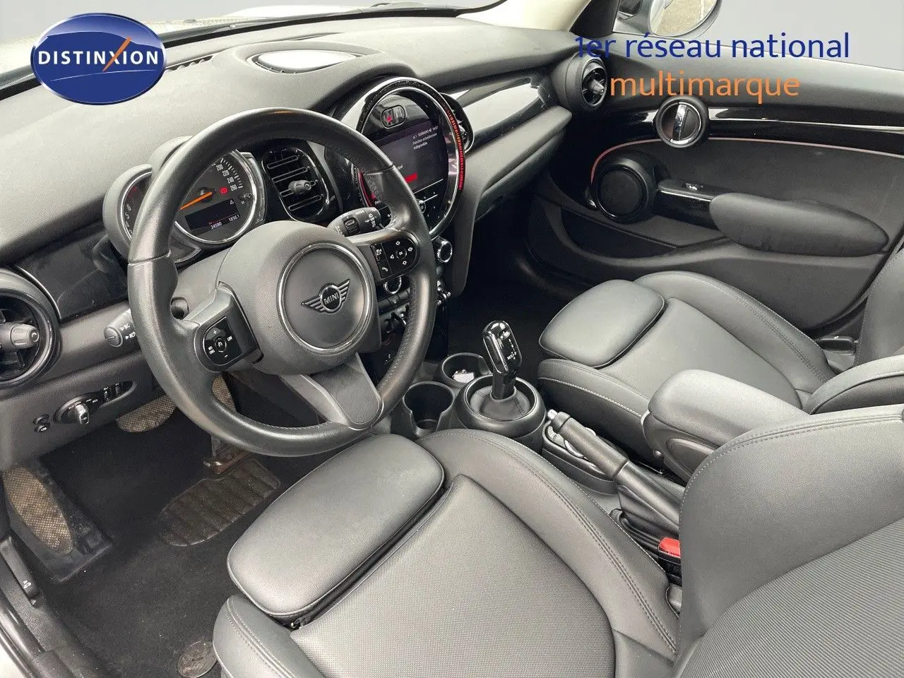 Vue intérieure côté conducteur de la MINI 1.5 136CH STEPTRONIC 2023 avec sièges cuir noir et tableau de bord moderne.