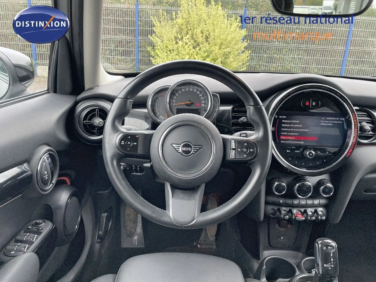 Vue intérieure centrée sur le volant et le tableau de bord d'une MINI 1.5 136CH STEPTRONIC noire, avec écran tactile rond.