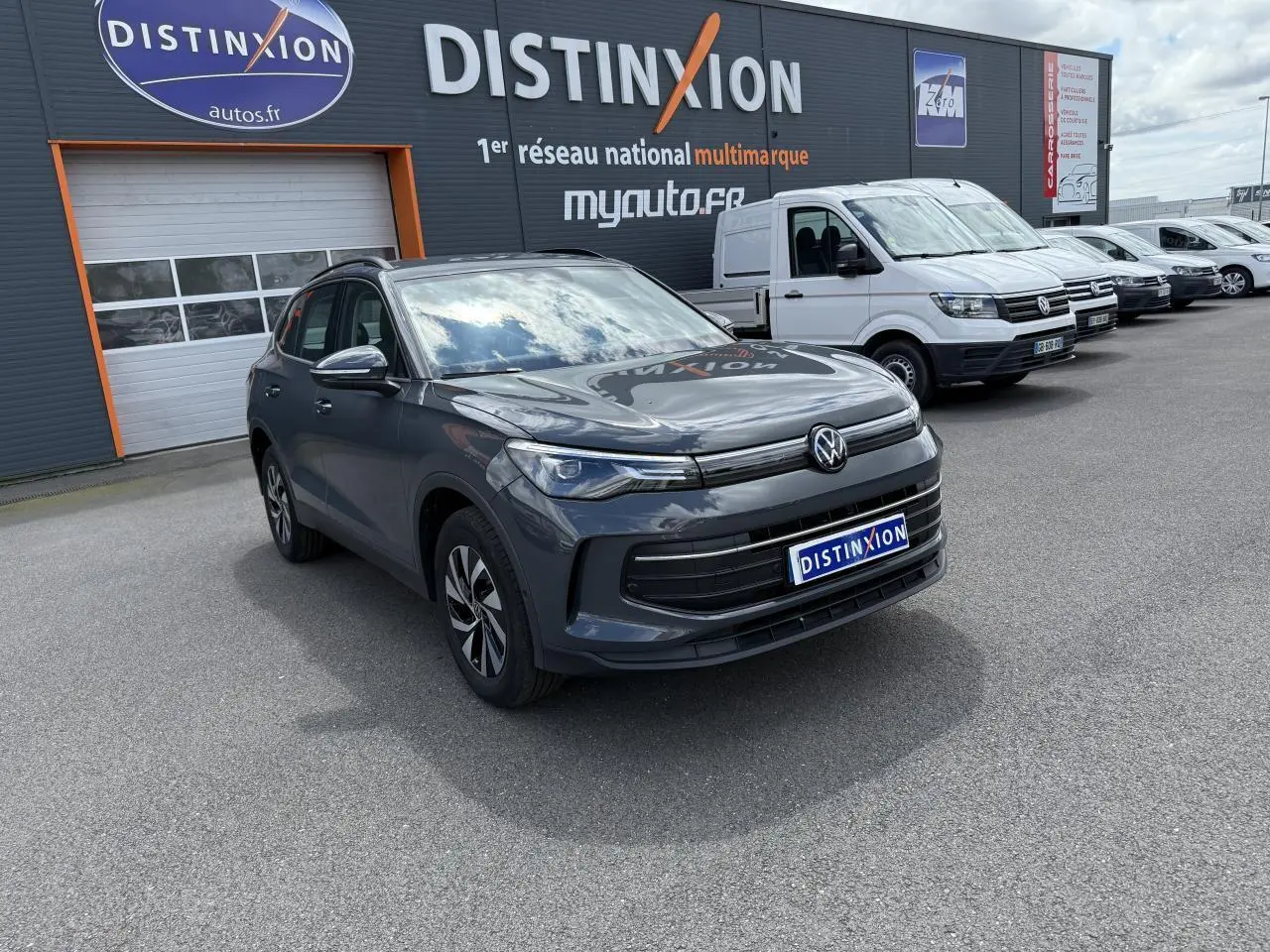 Volkswagen Tiguan 1.5 eHybrid gris dauphin vu en 3/4 avant sur parking devant un bâtiment Distinxion.