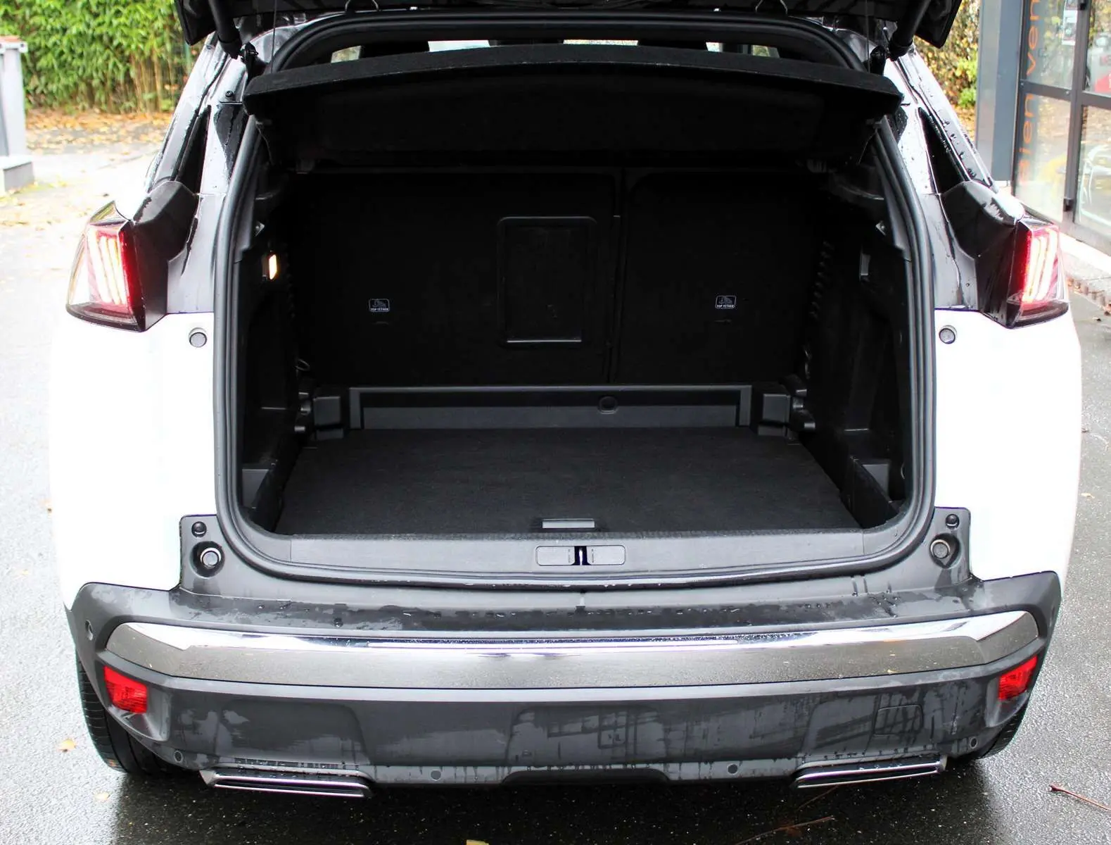 Vue arrière du Peugeot 3008 blanc nacré 2025 avec coffre ouvert et feux arrière allumés.