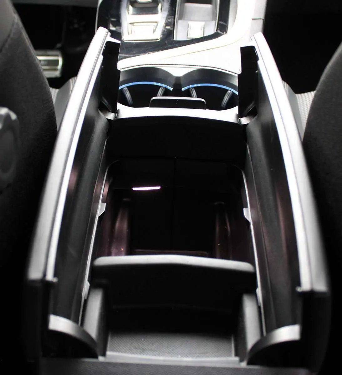 Vue rapprochée de la console centrale noire du Peugeot 3008 2025 avec porte-gobelets et rangement ouvert.