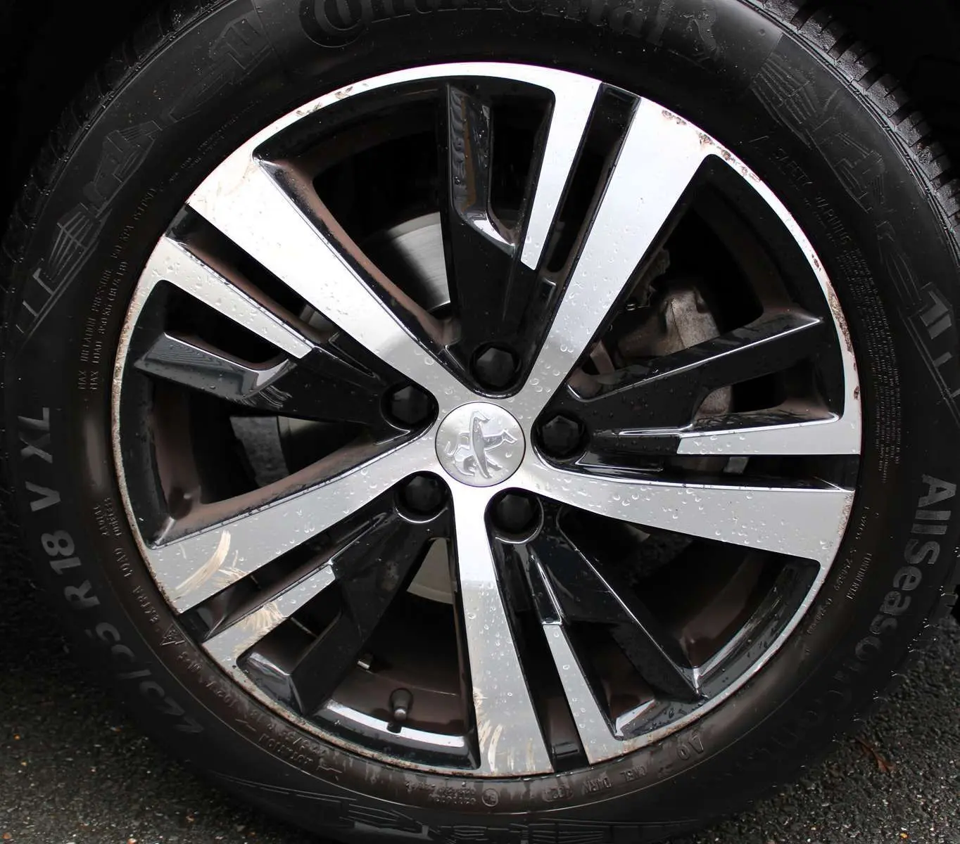 Gros plan sur la jante bi-ton noire et argentée avec logo Peugeot, montée sur un pneu Continental AllSeason.