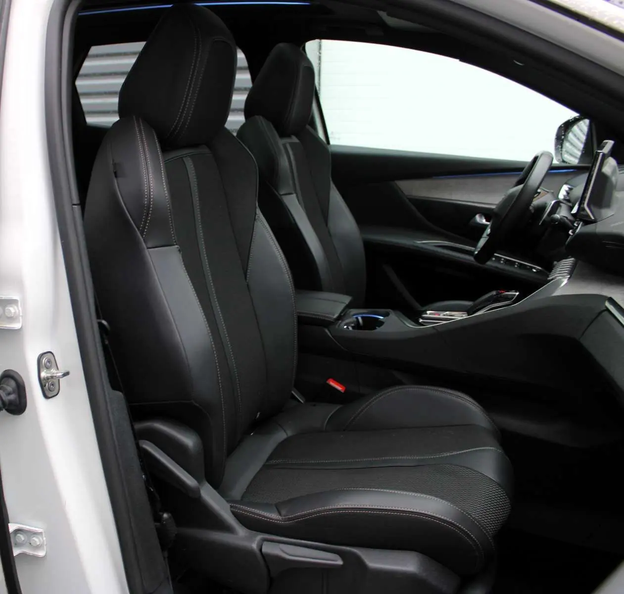 Vue intérieure côté conducteur du Peugeot 3008 blanc nacré 2025, sièges noirs en cuir et tableau de bord moderne.