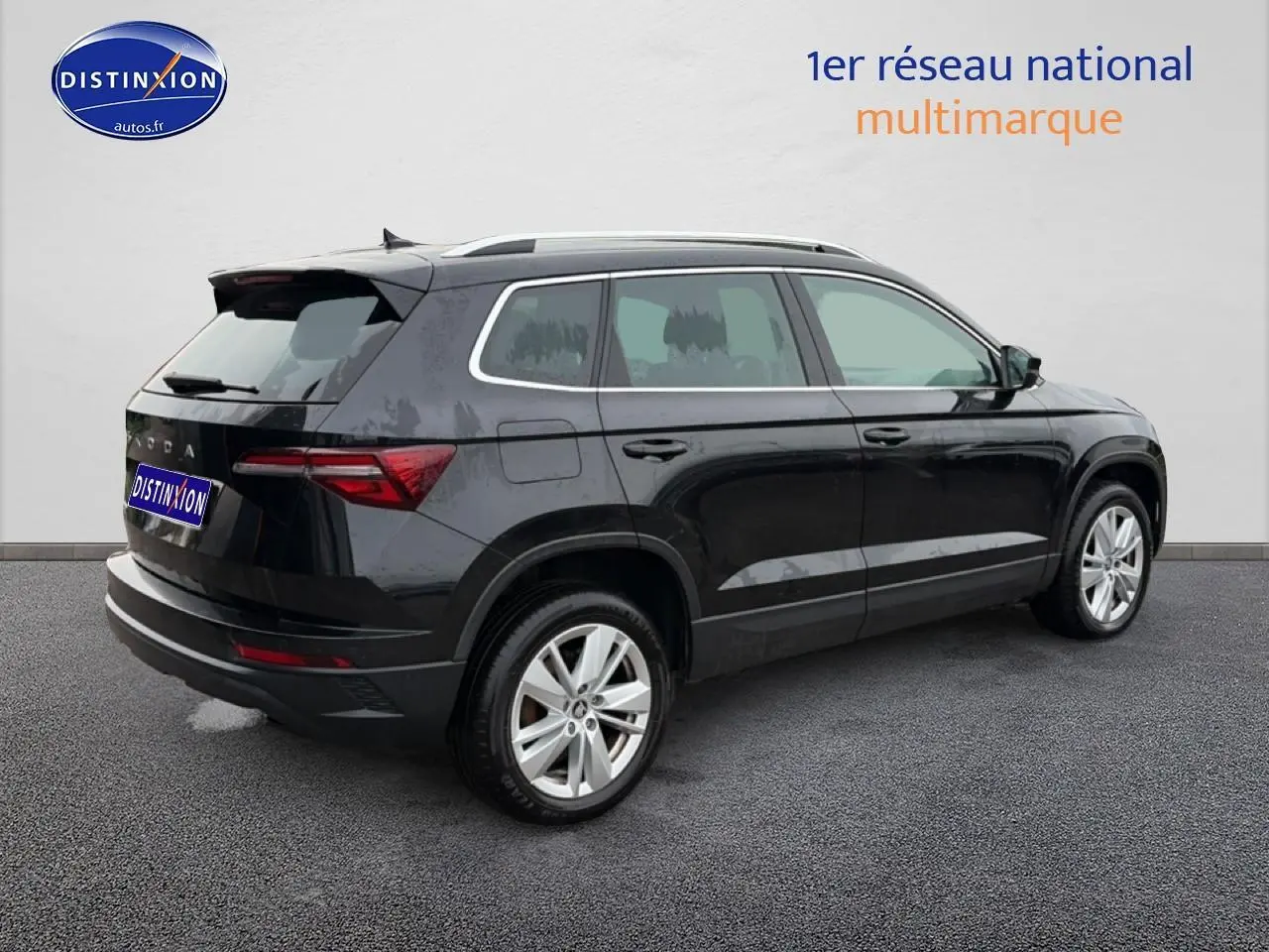 Vue 3/4 arrière droite d'un Skoda Karoq noir avec jantes alu et barres de toit sur fond neutre.