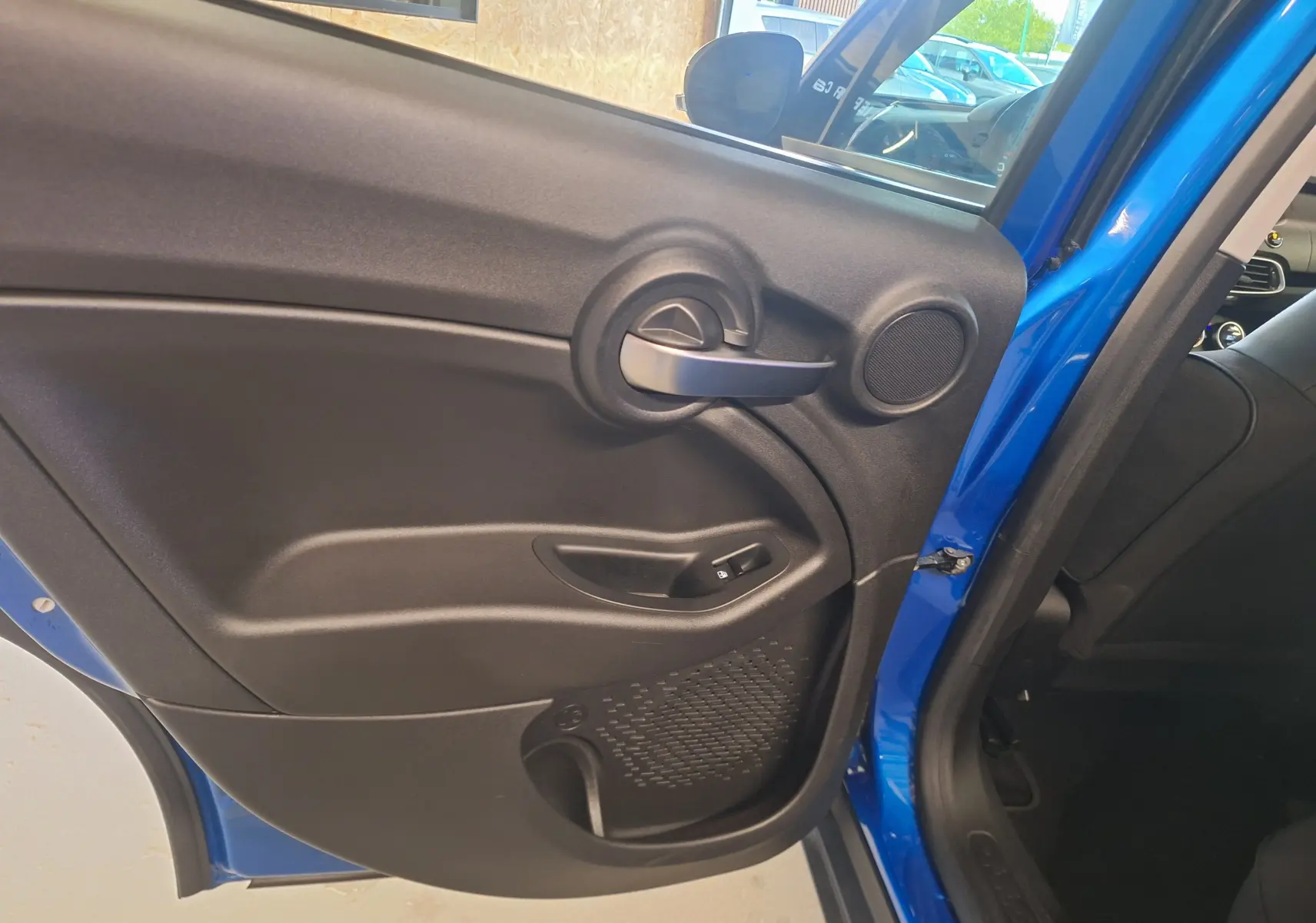 Gros plan sur la porte arrière côté gauche bleu métallisé du FIAT 500X 2024 avec poignée et haut-parleur intégrés.