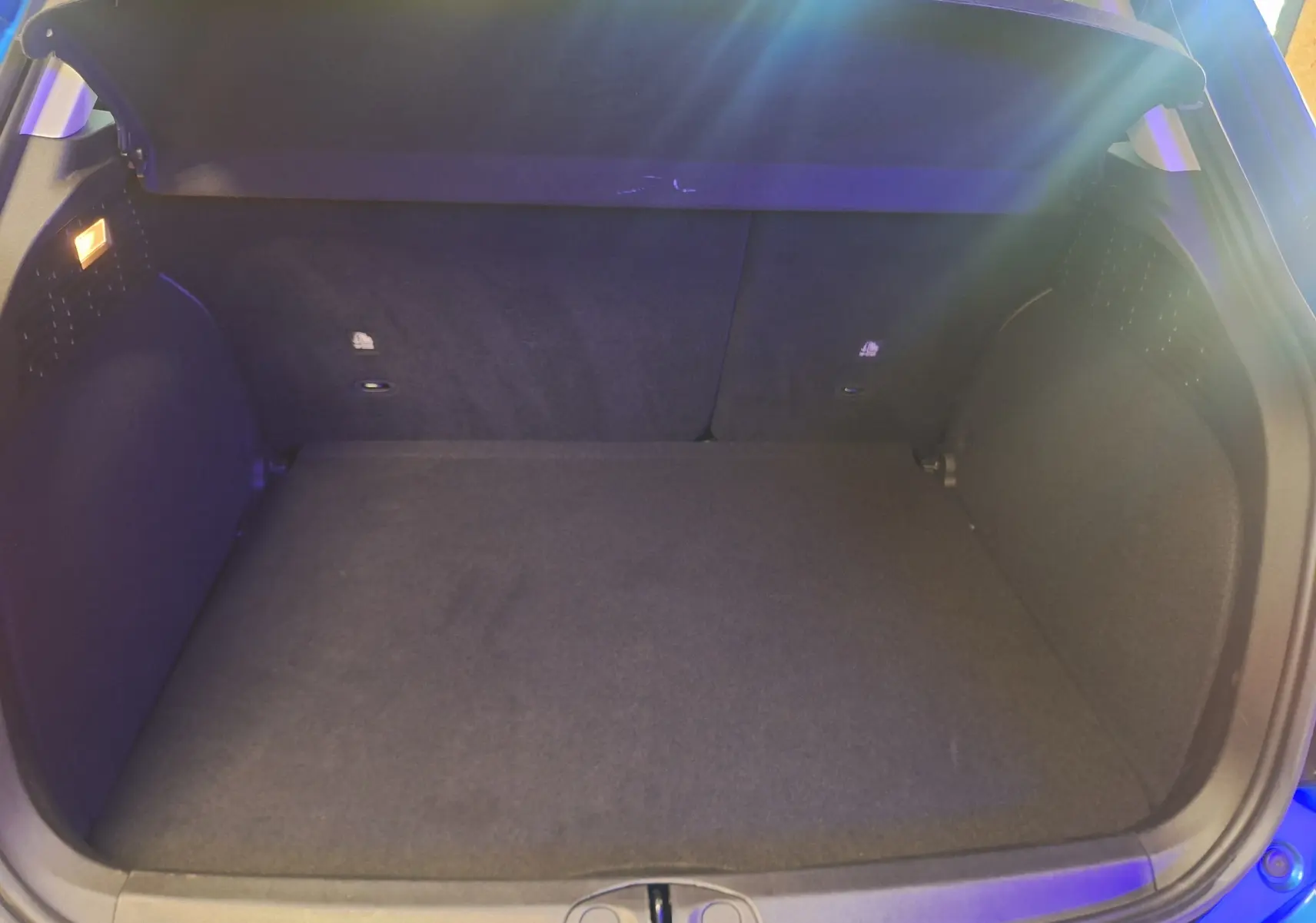 Coffre ouvert vu de l'arrière d'une FIAT 500X bleu, montrant l'espace de chargement et la moquette noire.