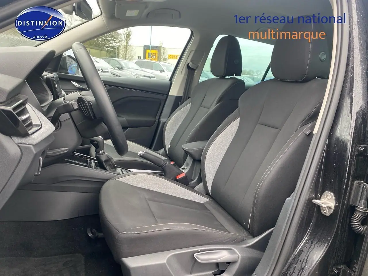 Vue intérieure côté conducteur du Skoda Kamiq noir 2025, sièges tissu bicolore avec accoudoir central et volant cuir multifonction.