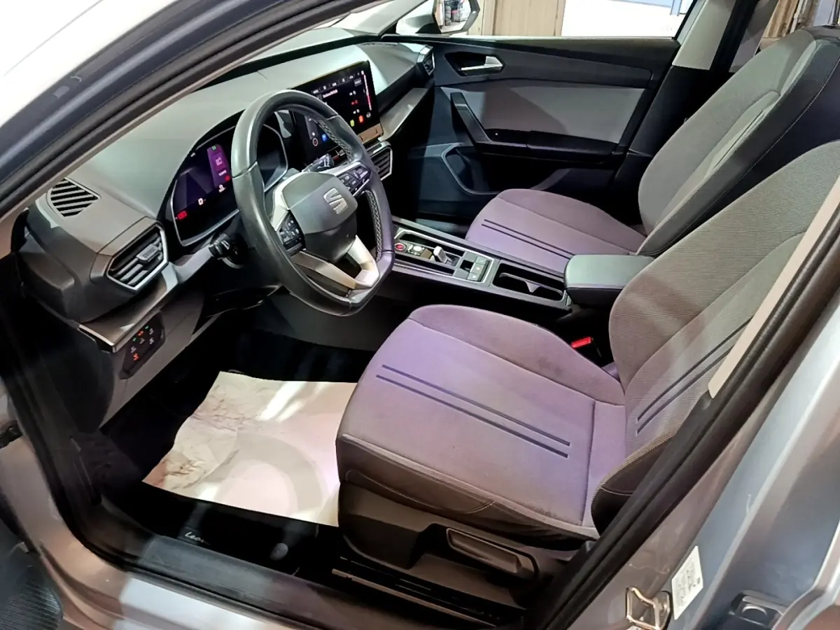 Vue intérieure côté conducteur de la SEAT Leon gris foncé 2022, avec tableau de bord digital et sièges tissu gris.