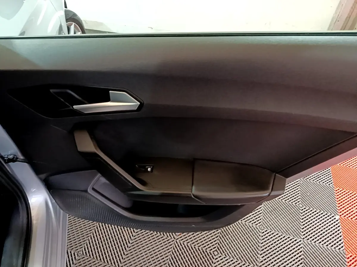 Vue rapprochée de la porte avant gauche grise foncée du SEAT LEON 2022, avec poignée argentée et accoudoir noir.