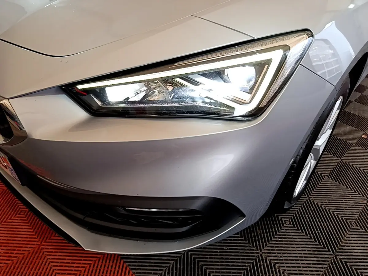 Gros plan sur le phare avant droit allumé d'une SEAT Leon gris foncé, avec partie de la roue visible.