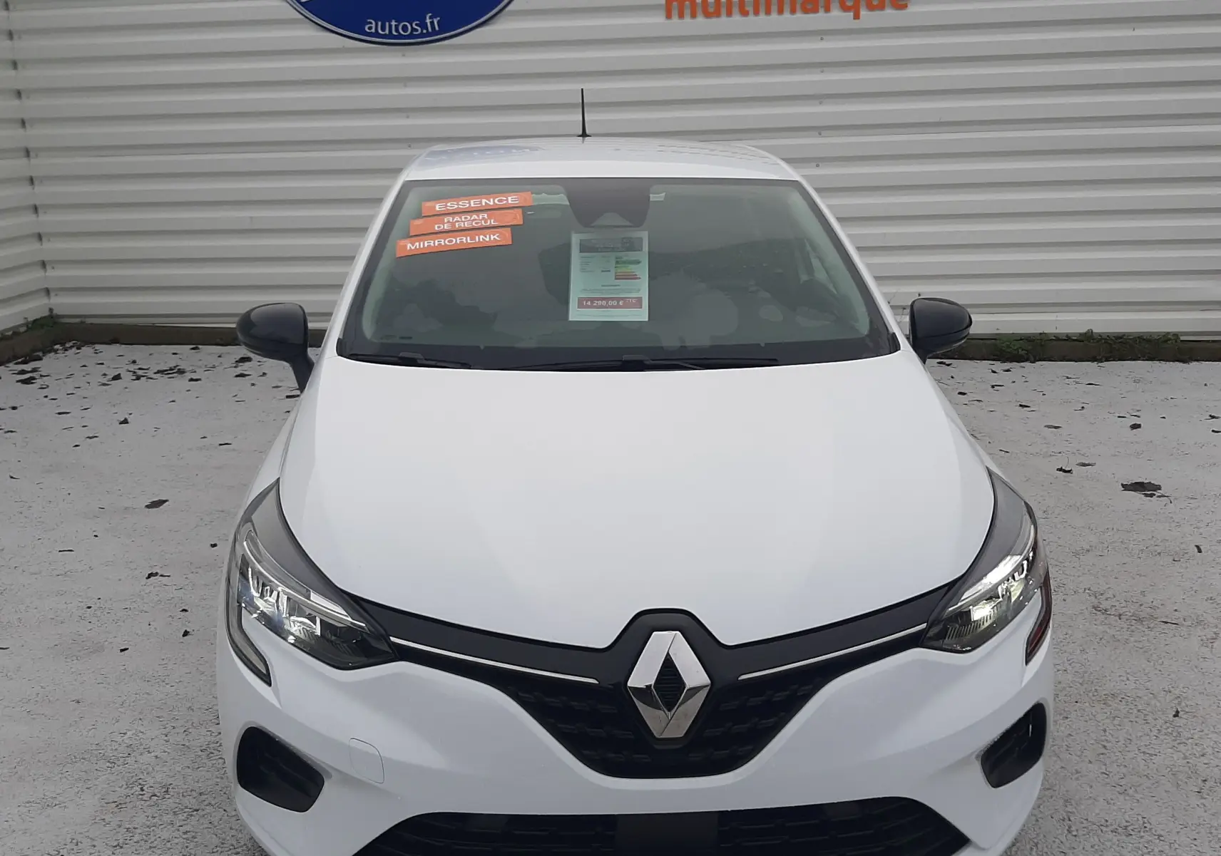 Vue avant d'une Renault Clio V blanche 2022 avec plaques "OCCASION" et autocollants sur le pare-brise.