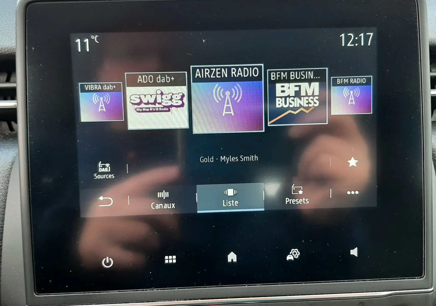 Écran tactile central de la Renault Clio V blanc, affichant les stations radio numériques avec commandes en dessous.