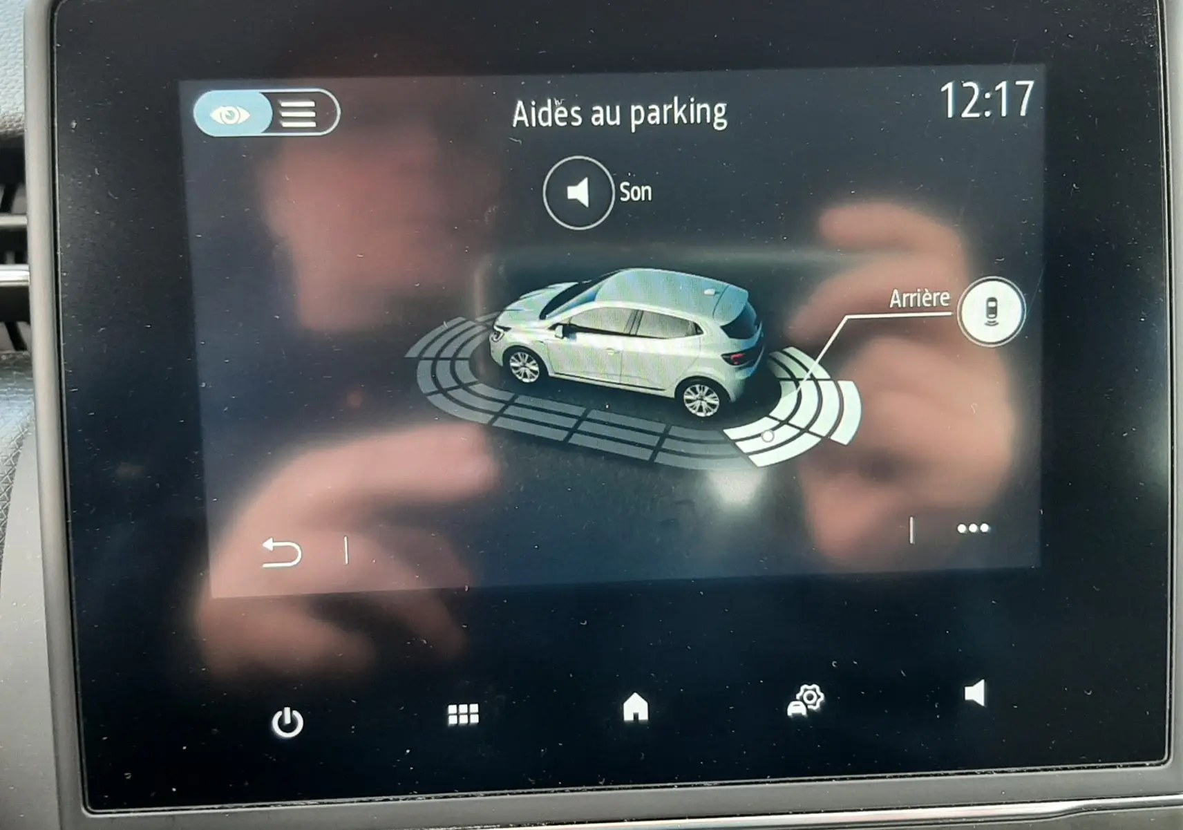 Écran tactile montrant l'aide au parking d'une Renault Clio V blanche vue en 3/4 arrière côté droit.