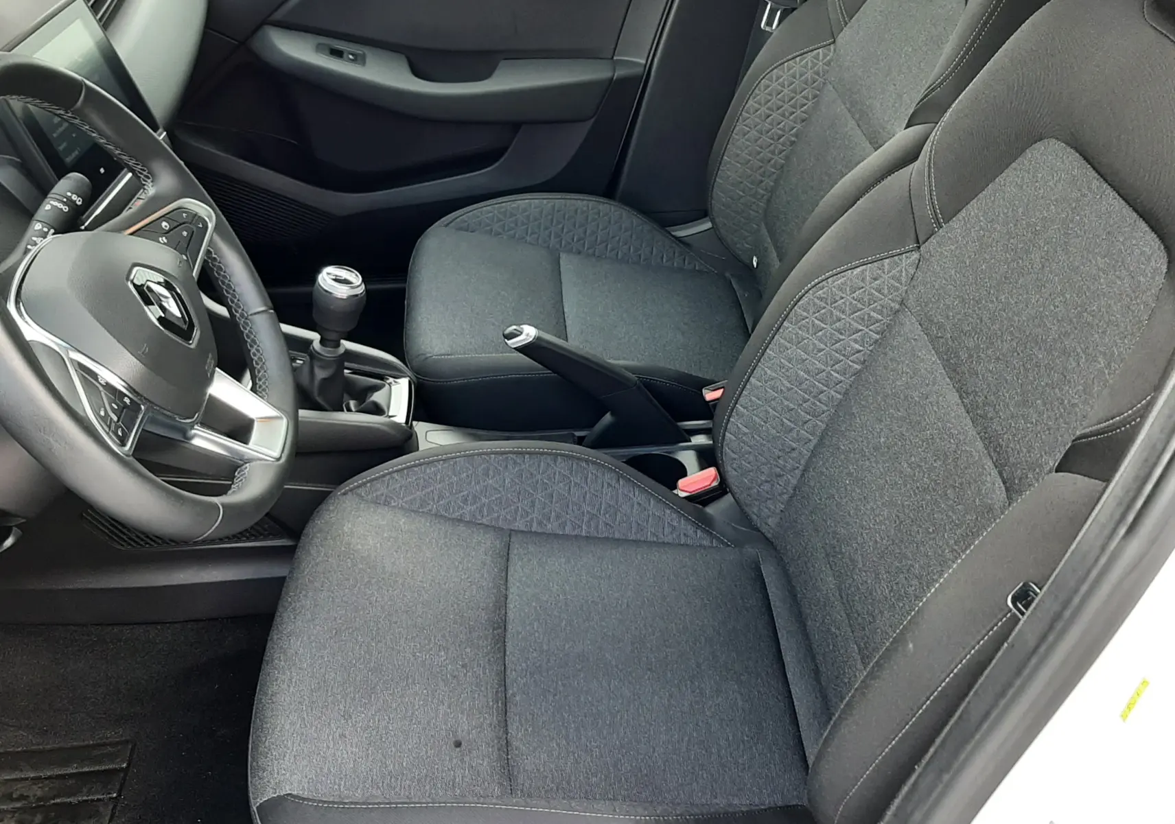 Vue intérieure côté conducteur de la Renault Clio V blanche, sièges tissu noir avec motifs géométriques et boîte manuelle.