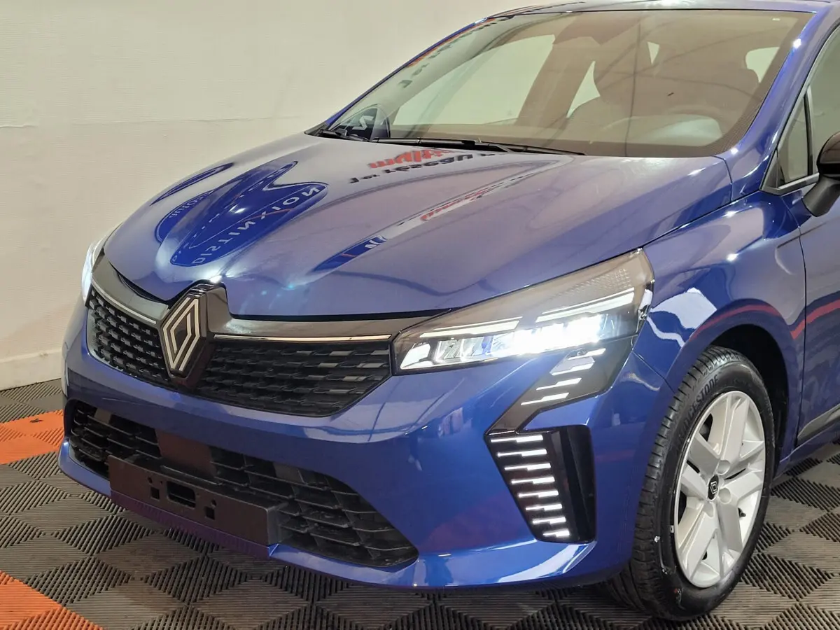 Vue 3/4 avant droit d'une Renault Clio Evolution Blue dCi 100 bleu avec phares LED allumés et jantes argentées.