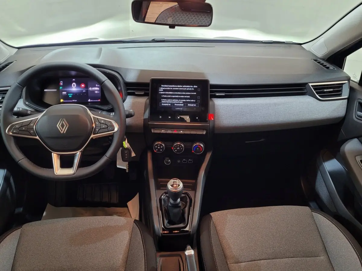 Vue intérieure avant de la Renault Clio 2025 avec tableau de bord gris, volant cuir multifonctions et boîte manuelle.