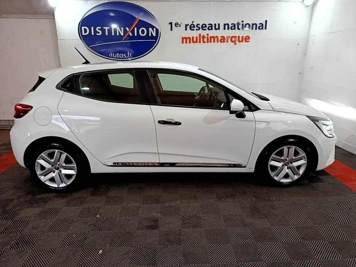 Profil droit d'une Renault Clio Business blanche de 2021, avec jantes alliage et rétroviseurs blancs dans un showroom.