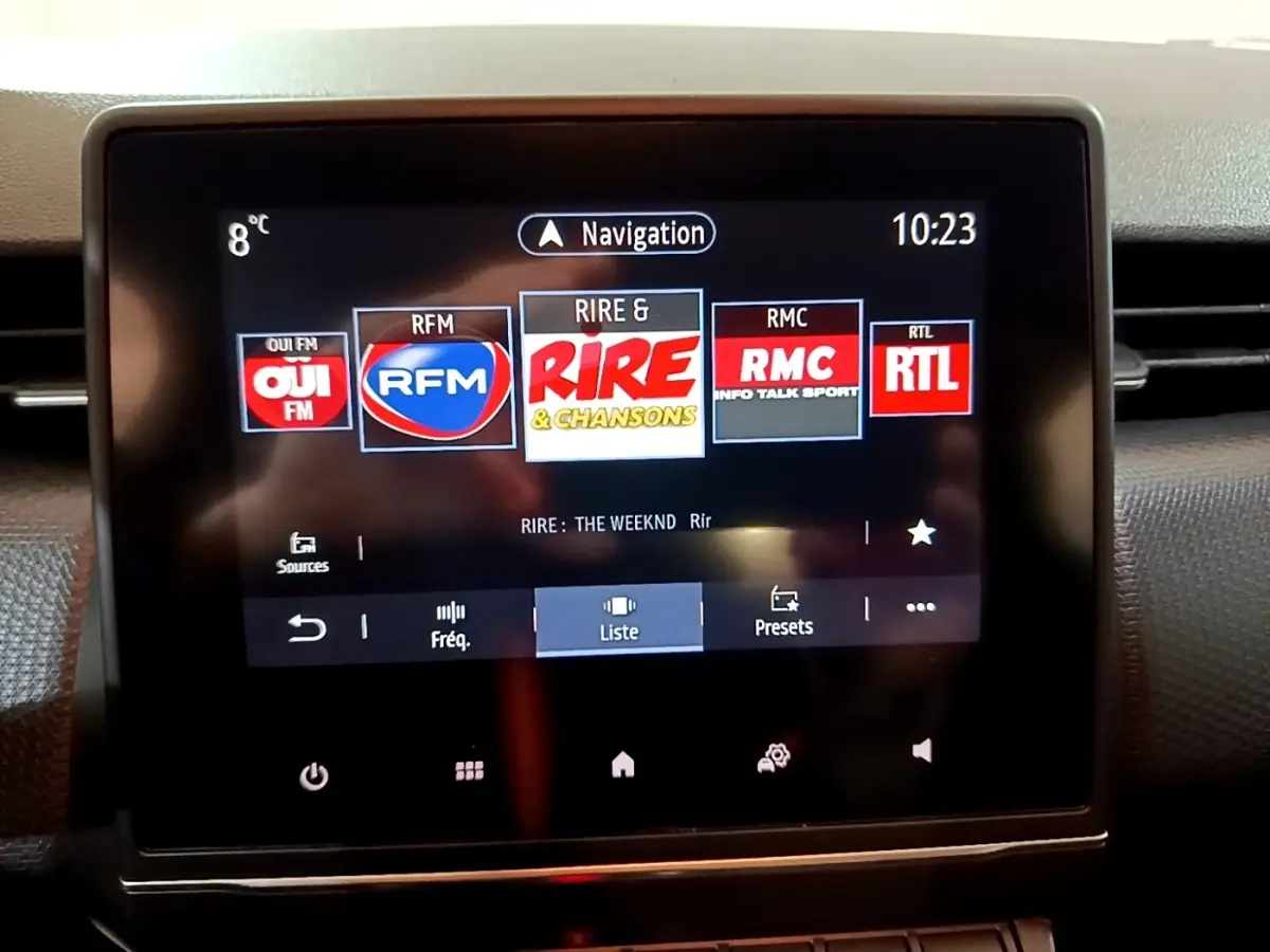 Écran tactile central du tableau de bord de la Renault Clio Business blanc, affichant les stations radio et la navigation.