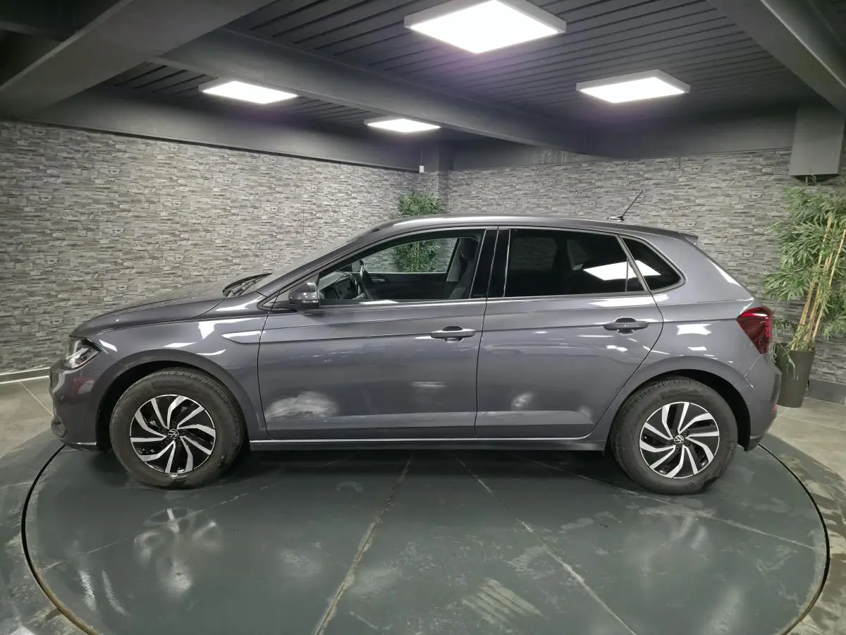 Profil côté gauche d'une Volkswagen Polo gris métallisé 2025 avec jantes alliage et vitres arrière surteintées dans un showroom.