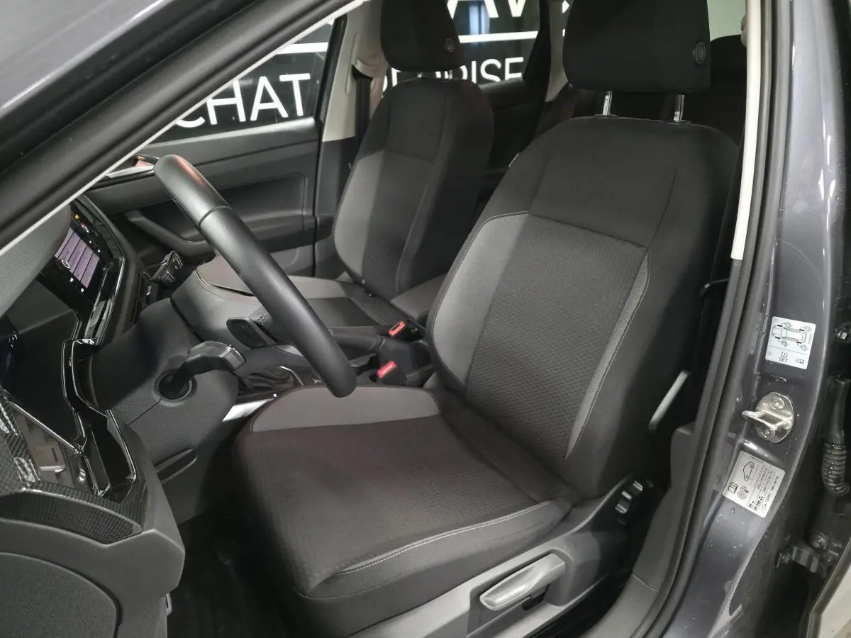 Vue intérieure côté conducteur de la Volkswagen Polo gris, montrant les sièges en tissu et le volant multifonction cuir.