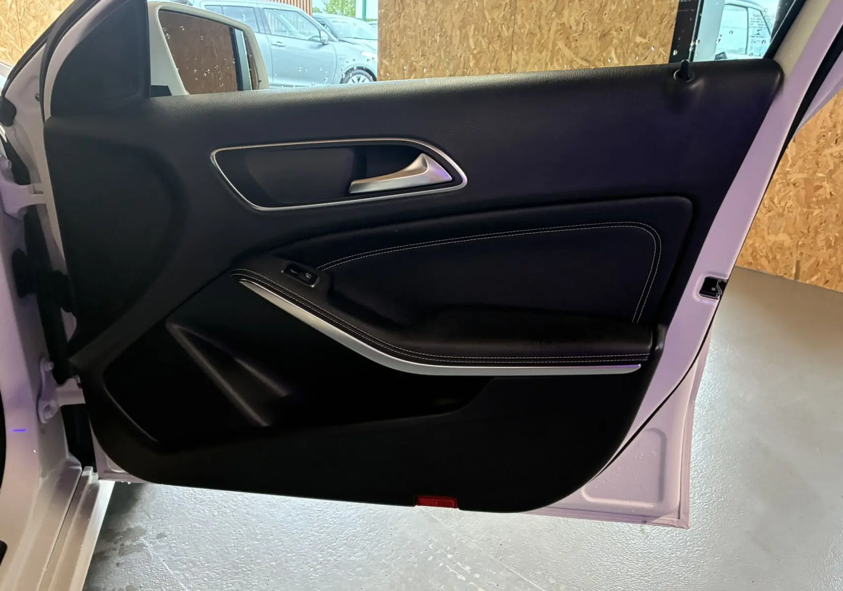 Porte avant gauche ouverte d'une Mercedes Classe A 200D blanche, montrant le panneau intérieur noir avec surpiqûres blanches.