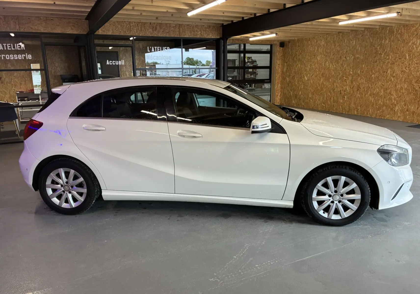 Profil droit d'une Mercedes Classe A 200D blanche de 2016, compacte et élégante, stationnée en intérieur.