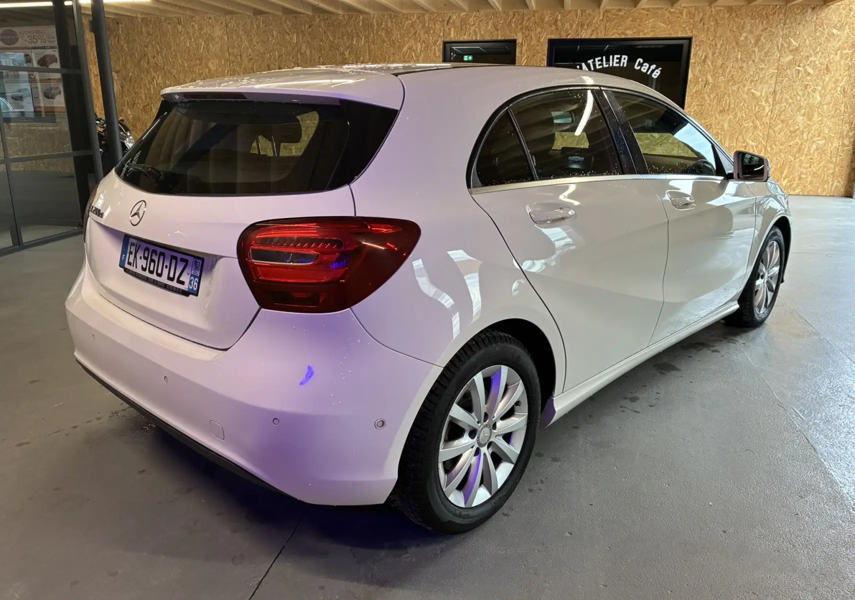 Mercedes Classe A 200D blanc vue 3/4 arrière droit en intérieur, avec feux arrière et jantes visibles.
