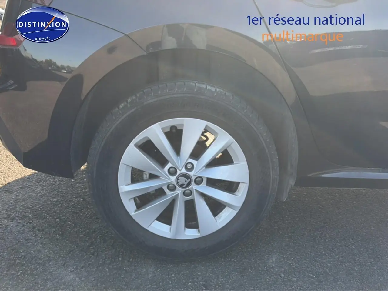 Gros plan sur la roue arrière droite d'un Skoda Kamiq noir avec jante alu et logo Skoda visible.